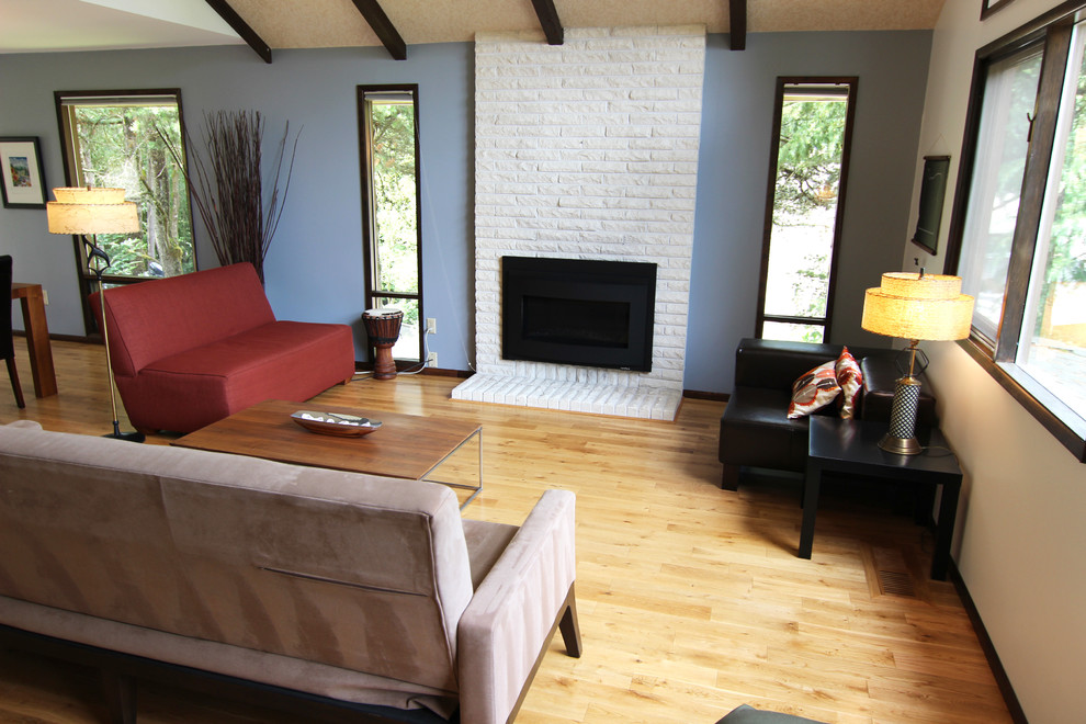 Modelo de salón abierto retro de tamaño medio sin televisor con paredes azules, todas las chimeneas, marco de chimenea de ladrillo, suelo marrón y suelo de madera clara