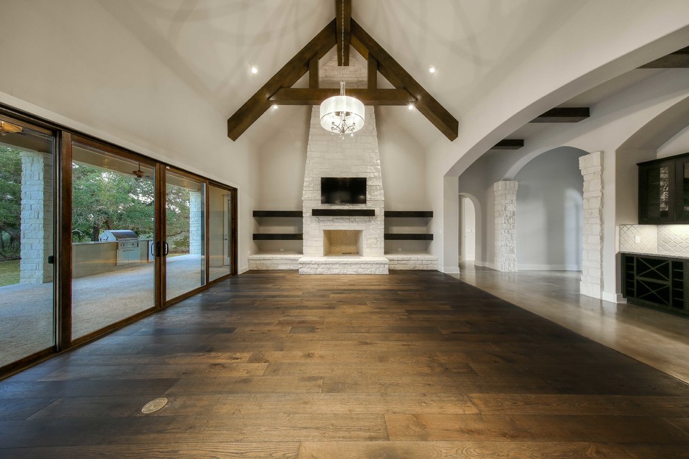 Cette image montre un grand salon traditionnel ouvert avec un mur blanc, un sol en bois brun, une cheminée standard, un manteau de cheminée en pierre et un téléviseur fixé au mur.