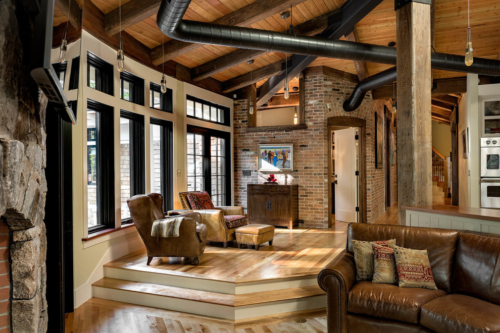 Mittelgroßes, Offenes Industrial Wohnzimmer mit beiger Wandfarbe, braunem Holzboden, Tunnelkamin und Kaminumrandung aus Stein in Boston