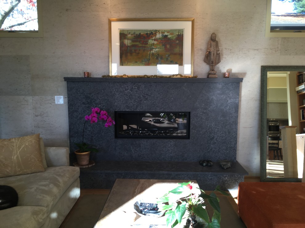 Cette image montre un salon design de taille moyenne et fermé avec un mur beige, un sol en calcaire, une cheminée standard, un manteau de cheminée en béton et un sol marron.
