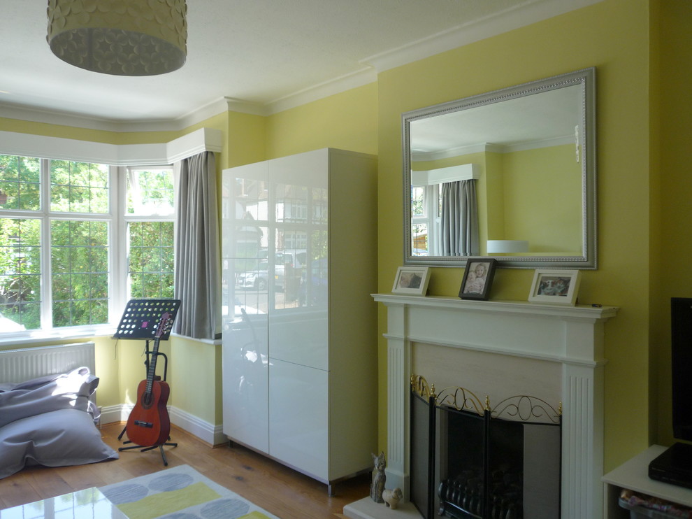 Exempel på ett mellanstort modernt separat vardagsrum, med gula väggar, mellanmörkt trägolv, en spiselkrans i trä, en väggmonterad TV och en standard öppen spis