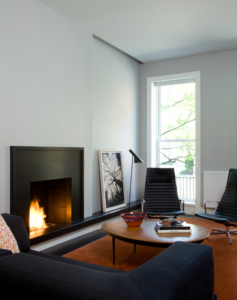 Cette image montre un salon minimaliste avec un mur blanc, une cheminée standard et canapé noir.
