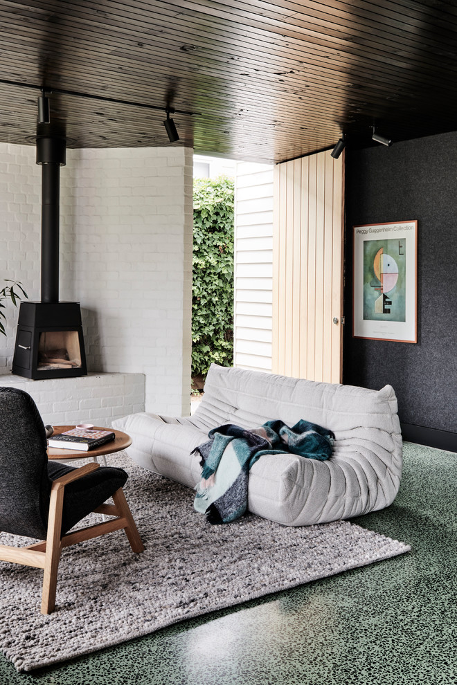 Ejemplo de salón abierto minimalista de tamaño medio con paredes blancas, suelo de cemento, estufa de leña, marco de chimenea de metal y suelo verde