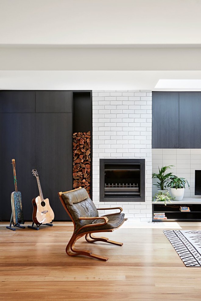 Cette image montre un salon design avec un mur blanc, un sol en bois brun, une cheminée standard, un manteau de cheminée en brique et un sol marron.