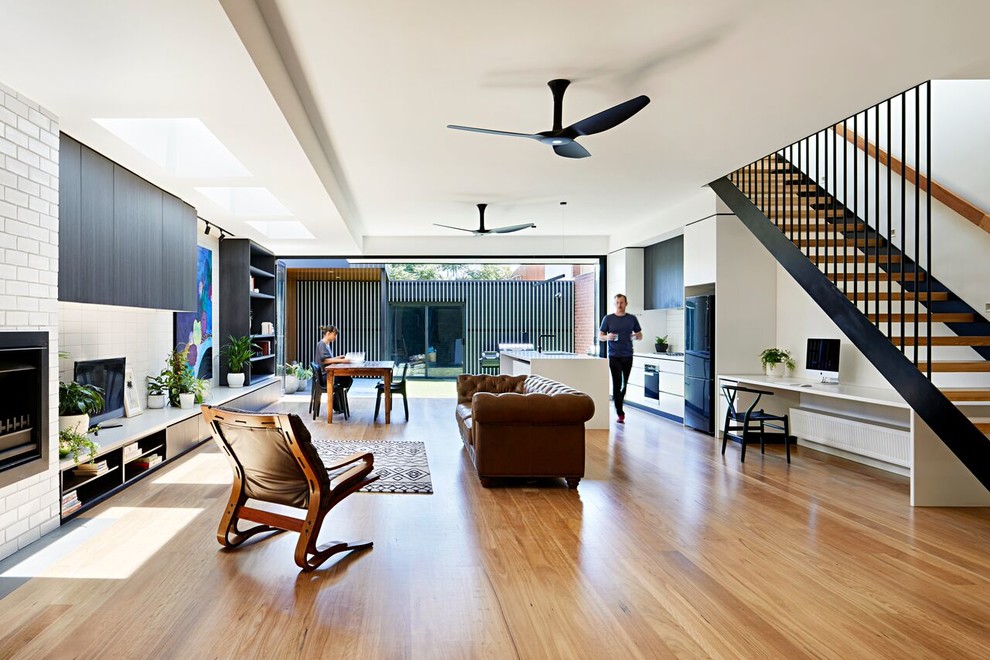 Offenes Modernes Wohnzimmer mit weißer Wandfarbe, braunem Holzboden, Kamin, Kaminumrandung aus Backstein, freistehendem TV und braunem Boden in Melbourne
