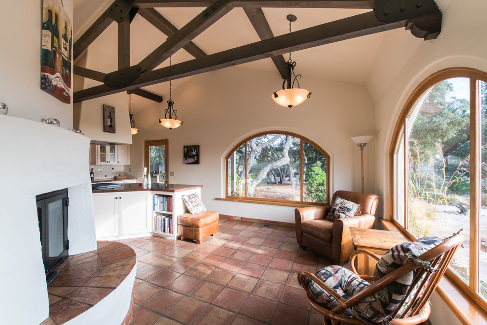 Photo of a mediterranean open plan living room in San Luis Obispo with white walls, terracotta flooring, a standard fireplace and brown floors.