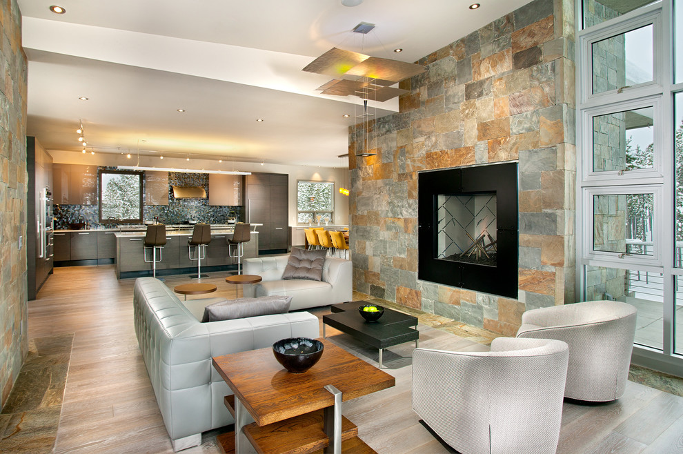 На фото: огромная открытая гостиная комната в современном стиле с домашним баром, светлым паркетным полом, серыми стенами, стандартным камином, фасадом камина из камня, серым полом и акцентной стеной без телевизора