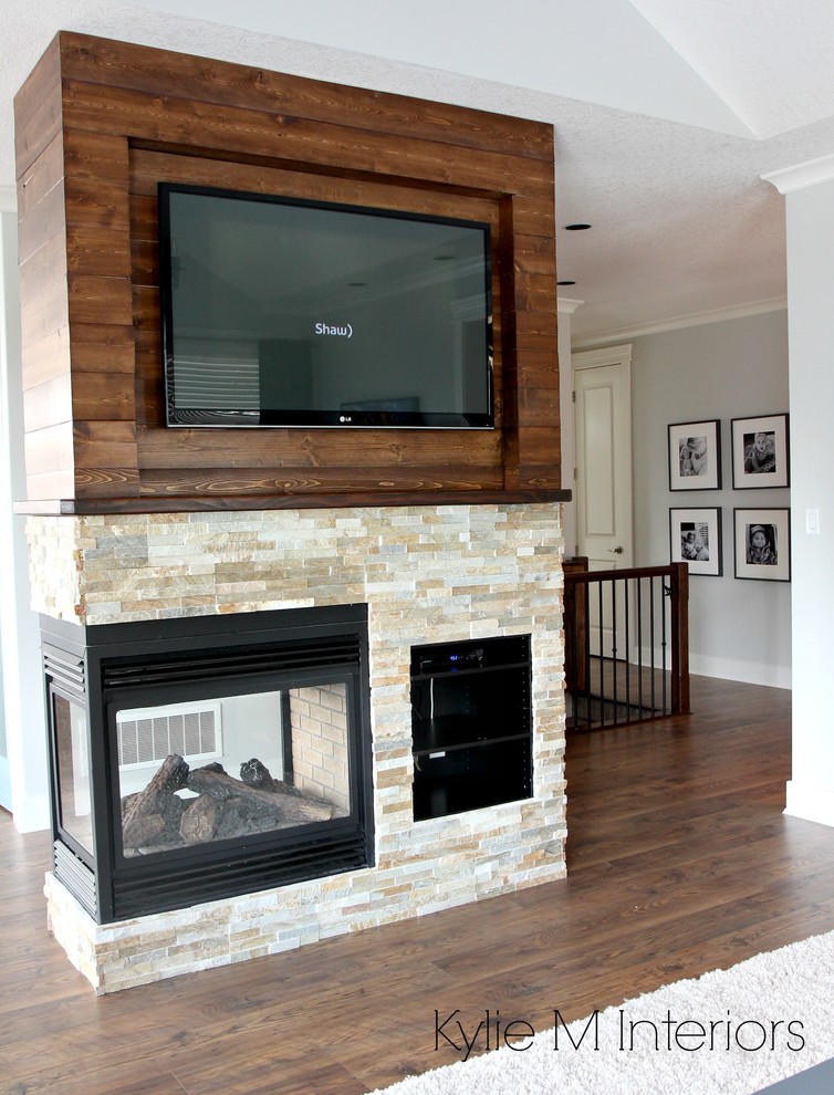 На фото: открытая гостиная комната среднего размера в стиле неоклассика (современная классика) с серыми стенами, полом из ламината, двусторонним камином, фасадом камина из камня, телевизором на стене и коричневым полом с