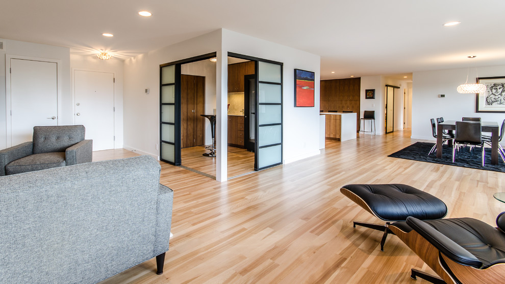 На фото: открытая гостиная комната в стиле модернизм с светлым паркетным полом, белыми стенами и телевизором на стене без камина