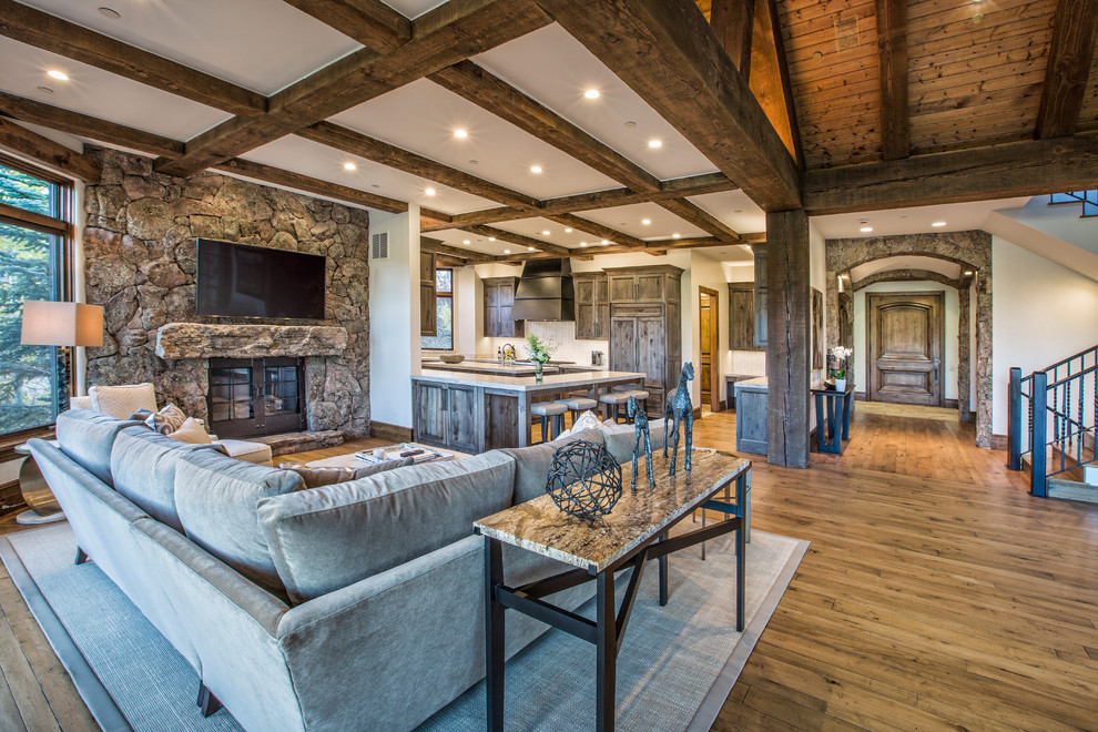 This is an example of a large rustic formal open plan living room in Denver with multi-coloured walls, light hardwood flooring, a standard fireplace, a stone fireplace surround, a wall mounted tv and brown floors.