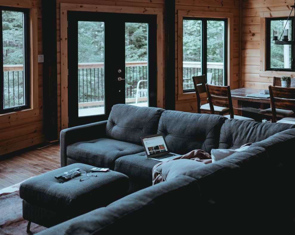 На фото: открытая гостиная комната в стиле рустика с коричневыми стенами, паркетным полом среднего тона, стандартным камином, телевизором на стене, коричневым полом, деревянным потолком и деревянными стенами с