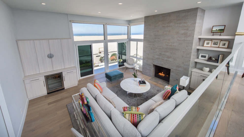 Inspiration for a large beach style open plan living room in Los Angeles with grey walls, medium hardwood flooring, a standard fireplace, a tiled fireplace surround and brown floors.
