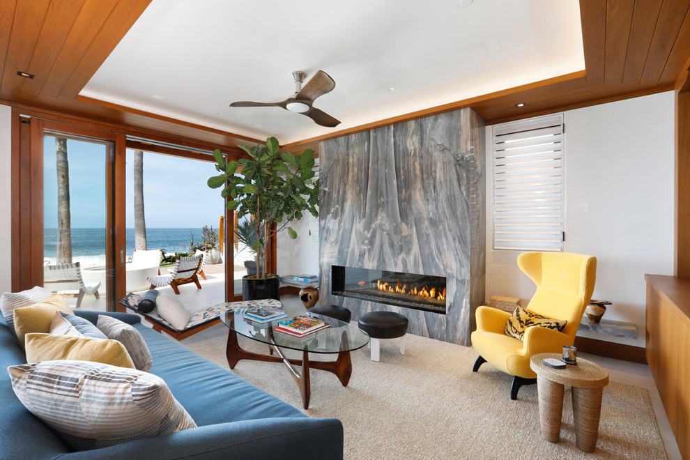 オレンジカウンティにある中くらいなビーチスタイルのおしゃれなLDK (白い壁、横長型暖炉、石材の暖炉まわり、コンクリートの床、テレビなし、ベージュの床、青いソファ) の写真