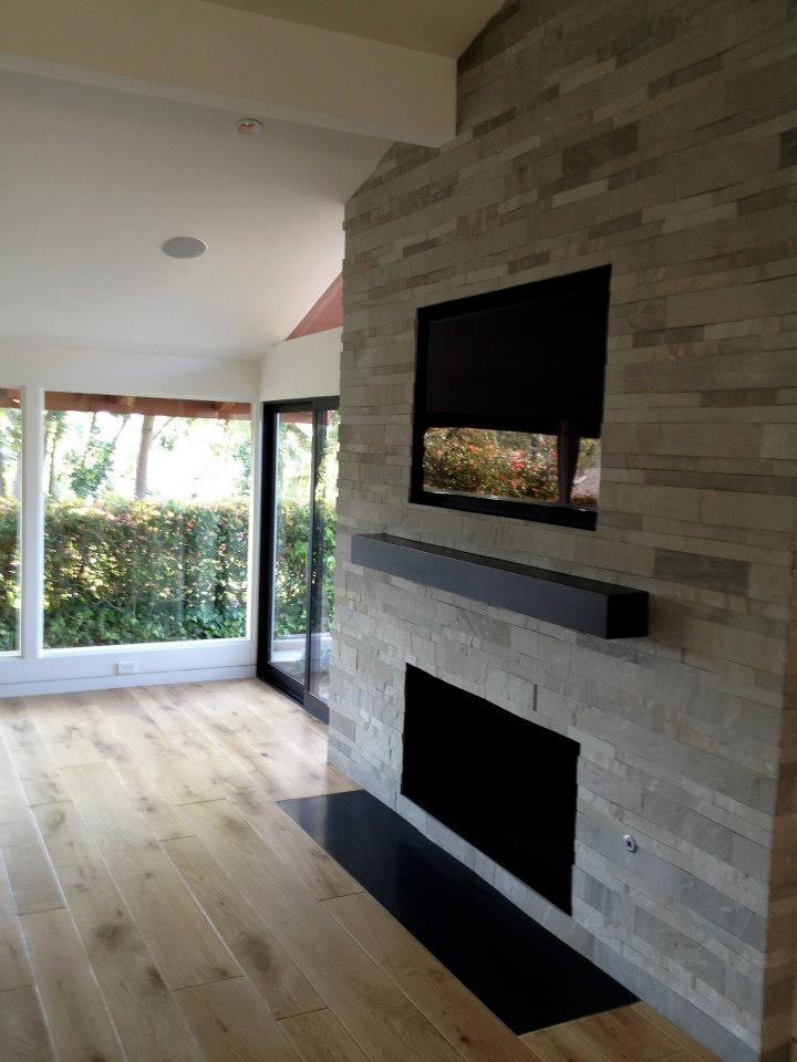 Foto de salón abierto contemporáneo con paredes grises, suelo de madera clara, televisor colgado en la pared, todas las chimeneas, marco de chimenea de piedra y suelo beige