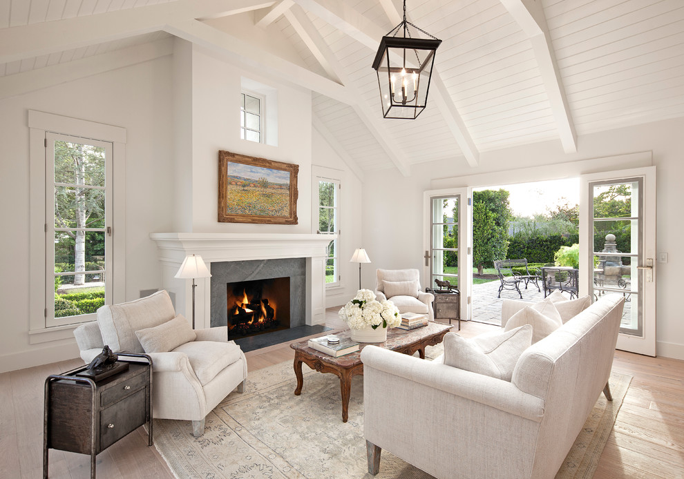 Classic formal open plan living room in Santa Barbara with white walls, light hardwood flooring, a standard fireplace, a stone fireplace surround and feature lighting.