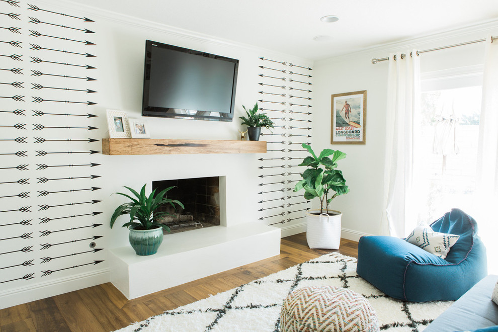 This is an example of a medium sized eclectic enclosed living room in Los Angeles with white walls, medium hardwood flooring, a standard fireplace, a wooden fireplace surround, a wall mounted tv and brown floors.