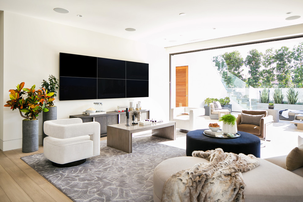 This is an example of a contemporary living room in Orange County with white walls, light hardwood flooring, a wall mounted tv and beige floors.