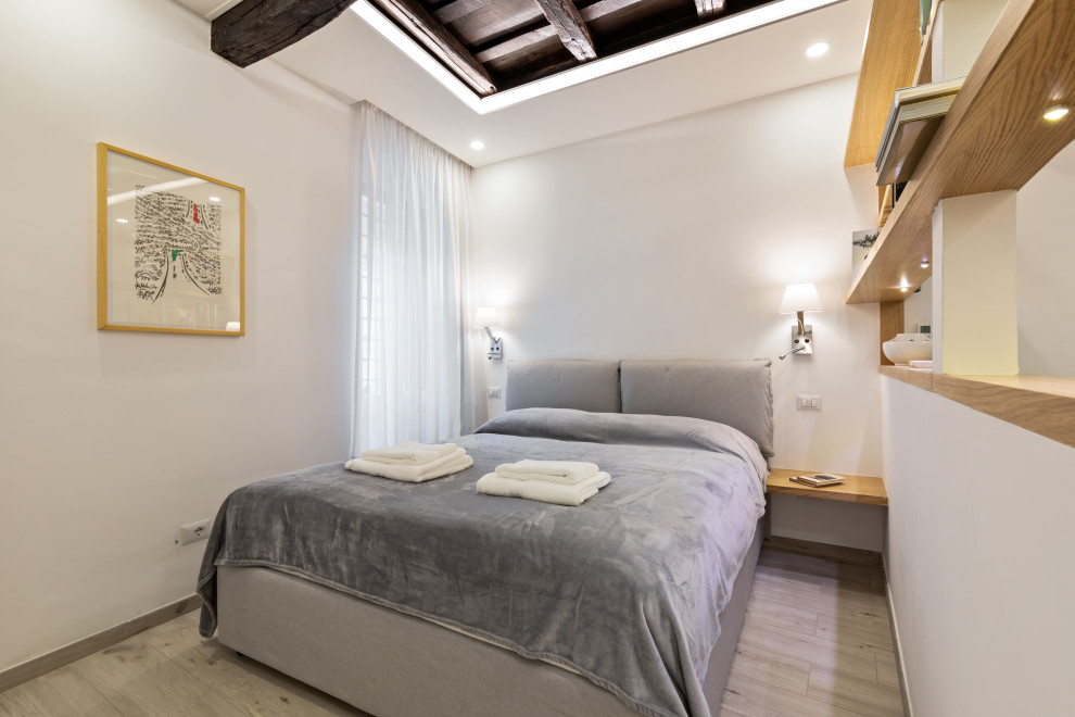 Inredning av ett modernt litet sovrum, med vita väggar, klinkergolv i porslin, en standard öppen spis, en spiselkrans i tegelsten och beiget golv