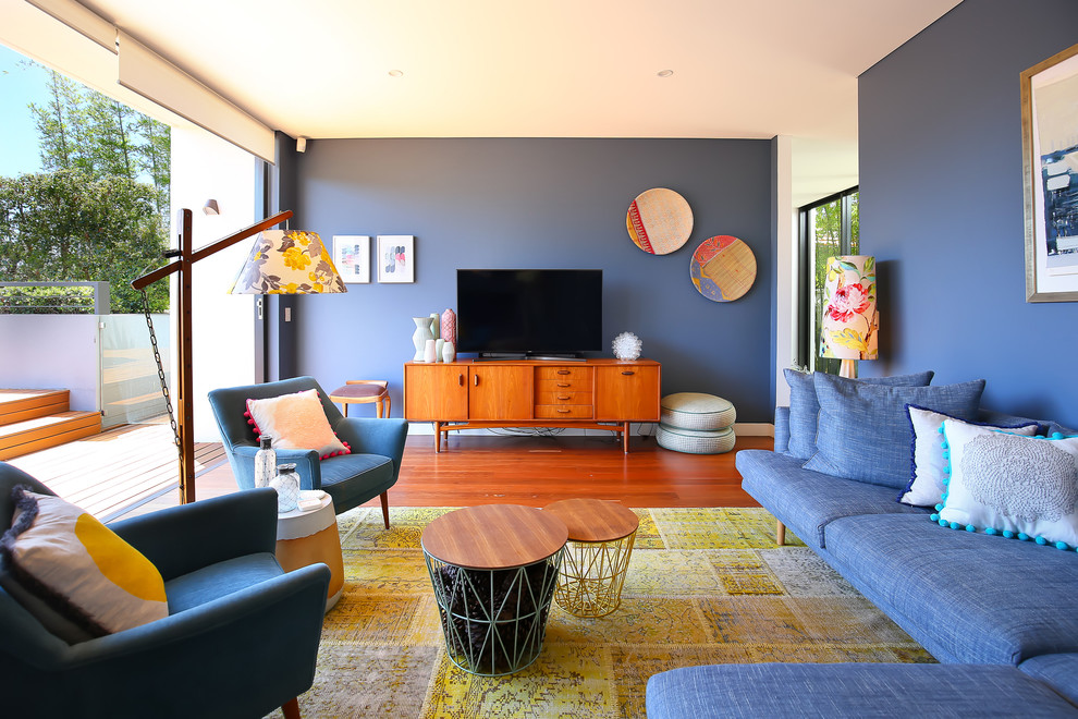 Mid-century modern enclosed medium tone wood floor living room photo in Sydney with blue walls and a tv stand