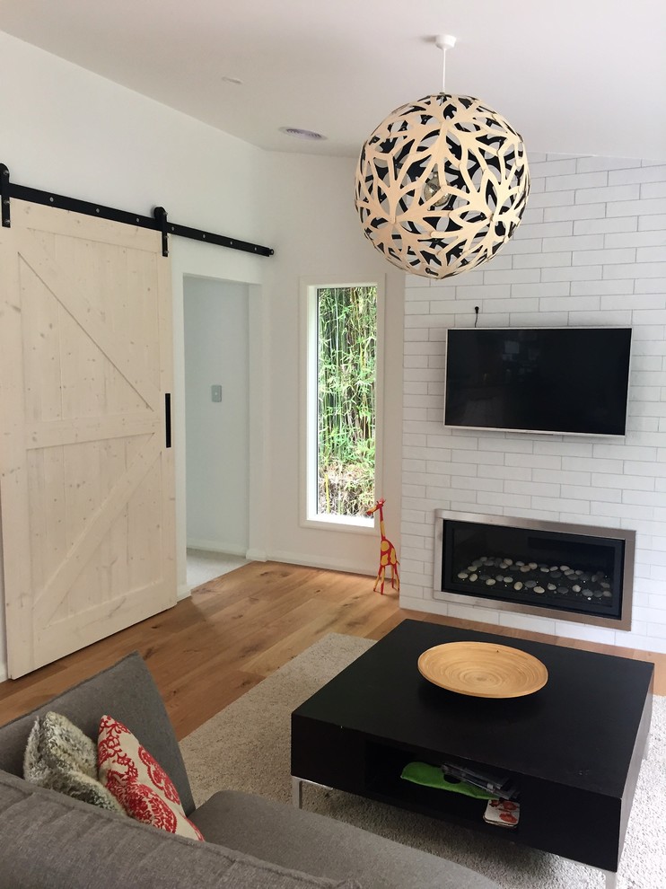 Mittelgroßes, Offenes Modernes Wohnzimmer mit weißer Wandfarbe, braunem Holzboden, Kamin, gefliester Kaminumrandung und TV-Wand in Auckland