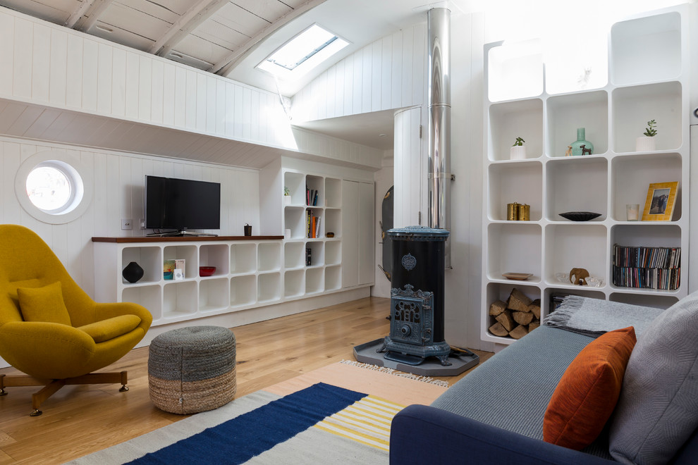 Diseño de salón cerrado retro de tamaño medio con paredes blancas, suelo de madera clara, estufa de leña y televisor independiente
