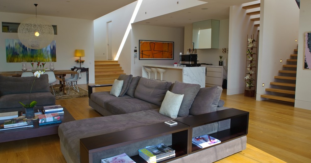 Modelo de salón abierto contemporáneo con paredes blancas, suelo de madera clara y televisor colgado en la pared