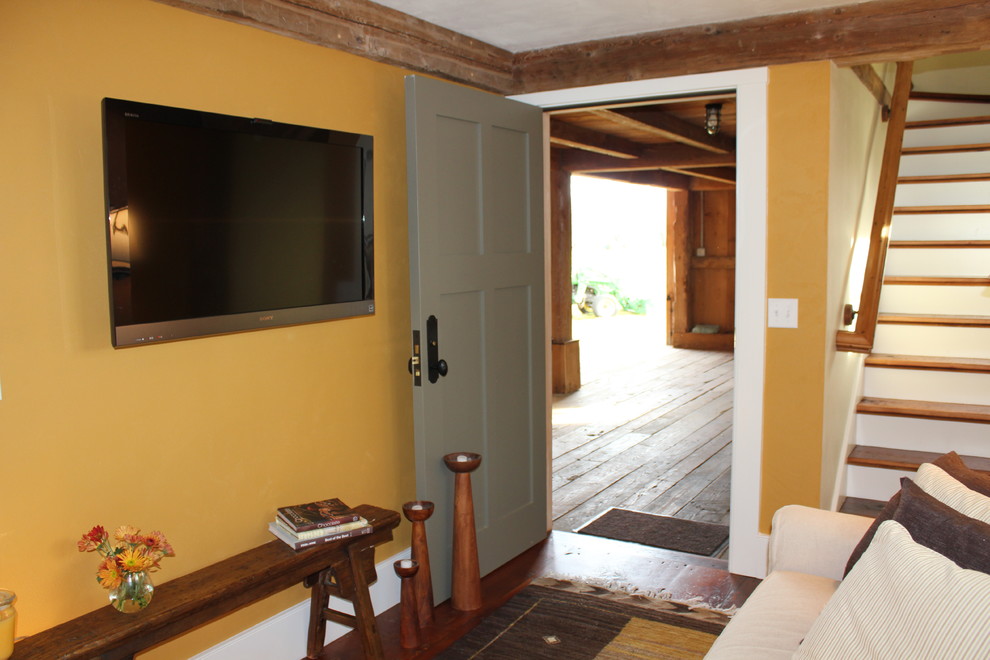 Diseño de salón cerrado campestre pequeño sin chimenea con televisor colgado en la pared, suelo de madera oscura y parades naranjas