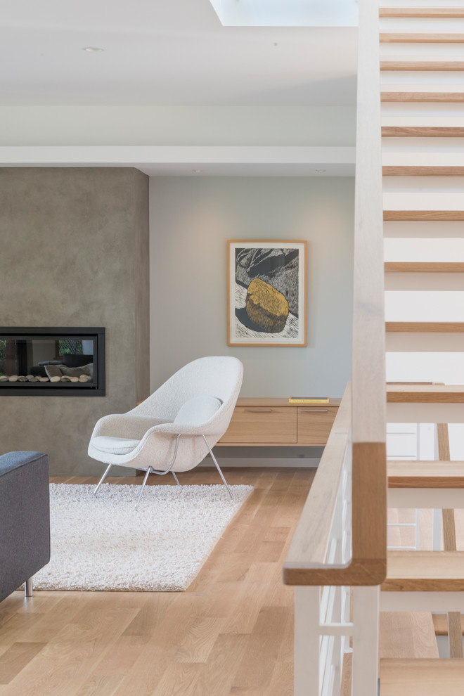 Esempio di un soggiorno minimalista di medie dimensioni e aperto con pareti grigie, parquet chiaro, camino classico e cornice del camino in intonaco