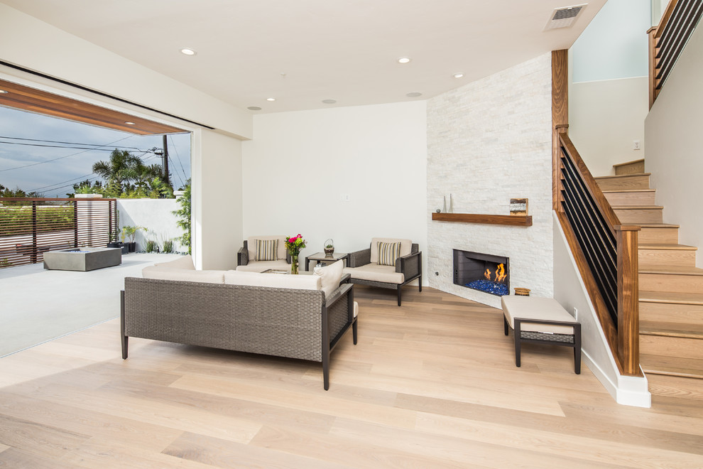 Пример оригинального дизайна: гостиная комната в современном стиле с серыми стенами, светлым паркетным полом, фасадом камина из камня и угловым камином без телевизора