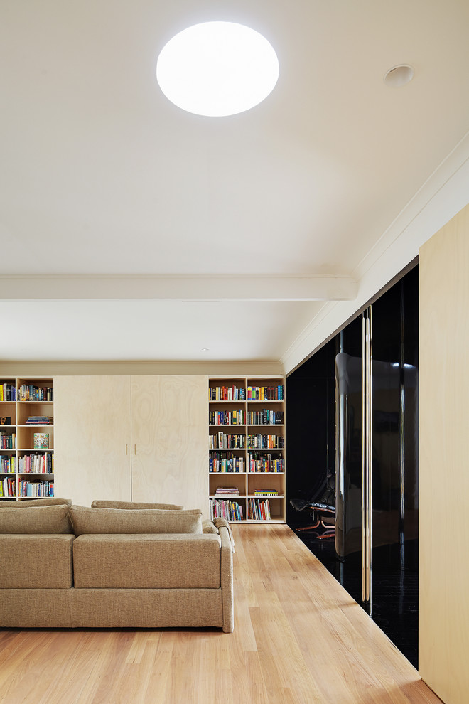Cette image montre un salon design avec une bibliothèque ou un coin lecture, un sol en bois brun, un téléviseur dissimulé et un mur beige.