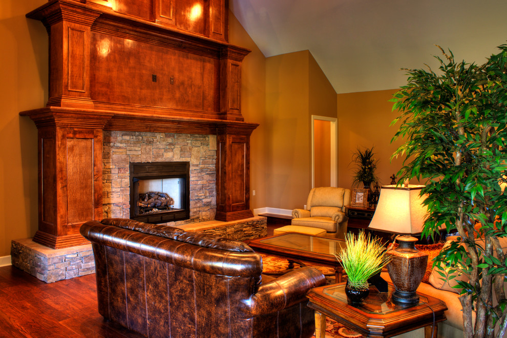 На фото: открытая, парадная гостиная комната в стиле кантри с телевизором на стене, коричневыми стенами, паркетным полом среднего тона, стандартным камином и фасадом камина из камня