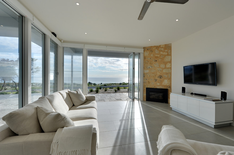 アデレードにある広いビーチスタイルのおしゃれなLDK (白い壁、セラミックタイルの床、コーナー設置型暖炉、石材の暖炉まわり、壁掛け型テレビ) の写真