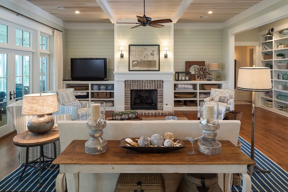 Inspiration for a large beach style enclosed living room in Atlanta with medium hardwood flooring, a standard fireplace, a brick fireplace surround, beige walls, a freestanding tv and feature lighting.