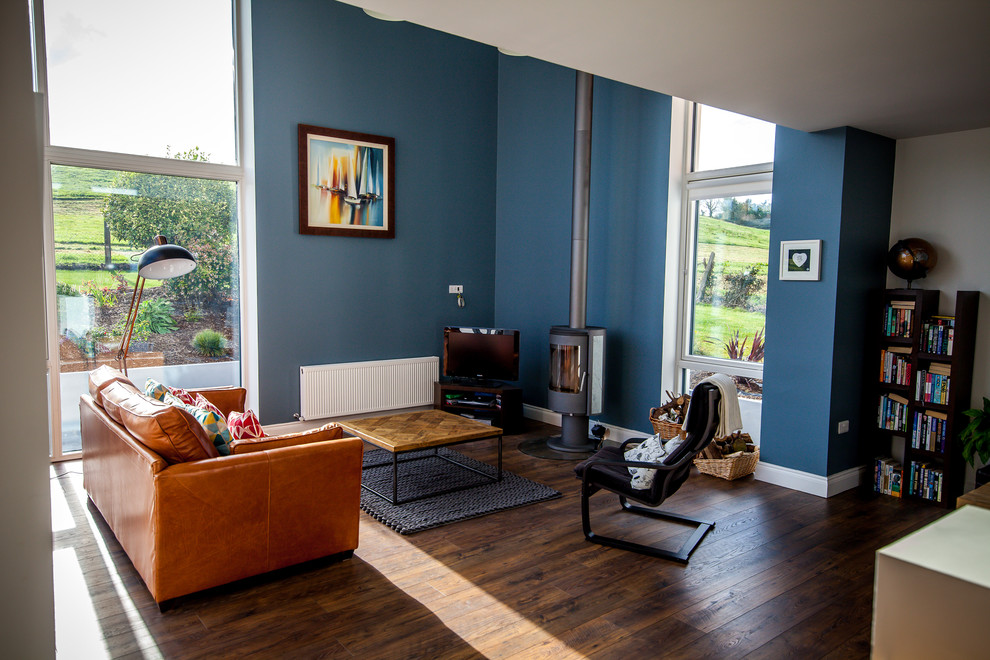 Bild på ett funkis allrum med öppen planlösning, med blå väggar, mörkt trägolv, en öppen vedspis och en fristående TV