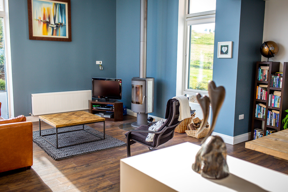 Diseño de salón abierto actual con paredes azules, suelo de madera oscura, estufa de leña y televisor independiente