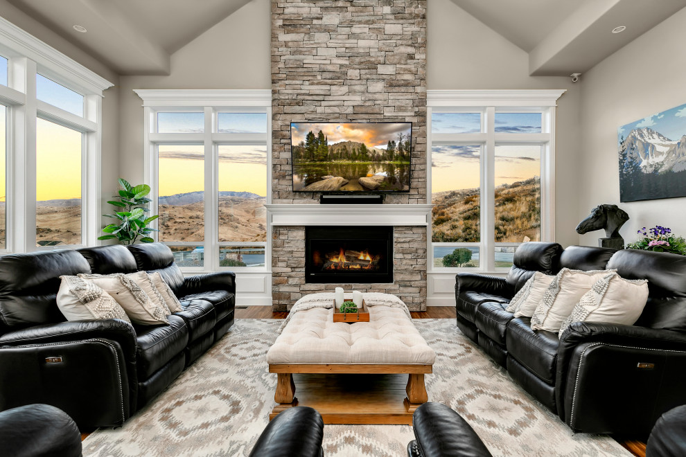 Пример оригинального дизайна: большая гостиная комната в стиле кантри с серыми стенами, паркетным полом среднего тона, стандартным камином, фасадом камина из камня, телевизором на стене и коричневым полом