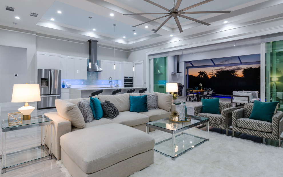 На фото: большая открытая гостиная комната в средиземноморском стиле с серыми стенами, полом из керамической плитки, телевизором на стене, серым полом и многоуровневым потолком