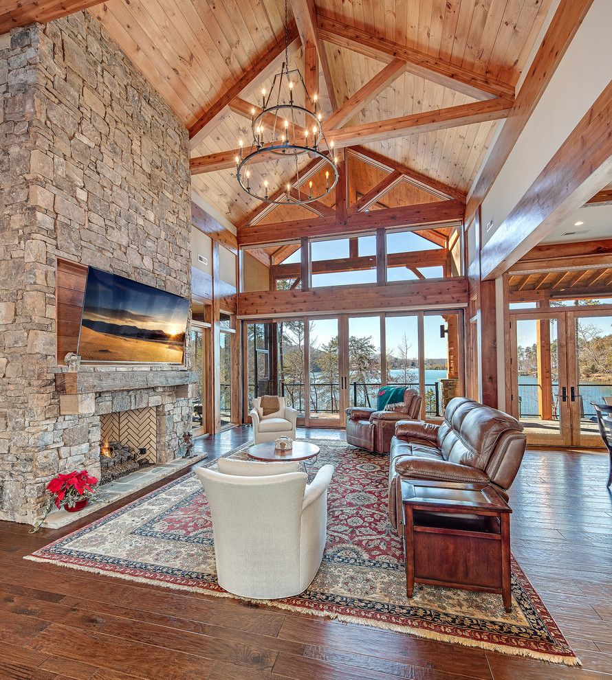 Medium sized rustic formal open plan living room with white walls, medium hardwood flooring, a standard fireplace, a stone fireplace surround, a wall mounted tv and brown floors.