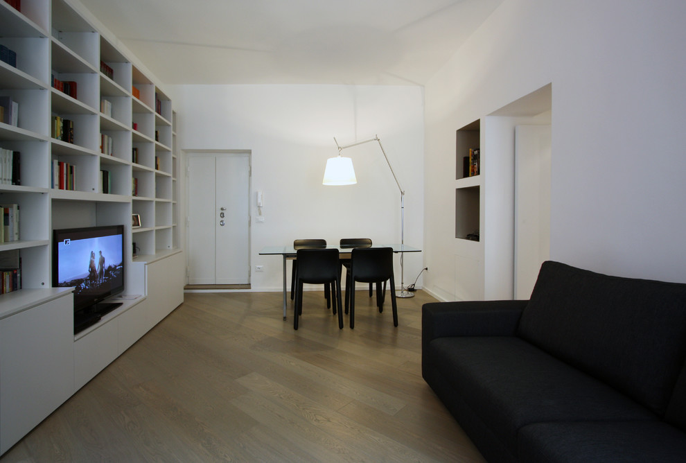 Modelo de biblioteca en casa abierta minimalista pequeña con paredes blancas, suelo de madera en tonos medios y pared multimedia