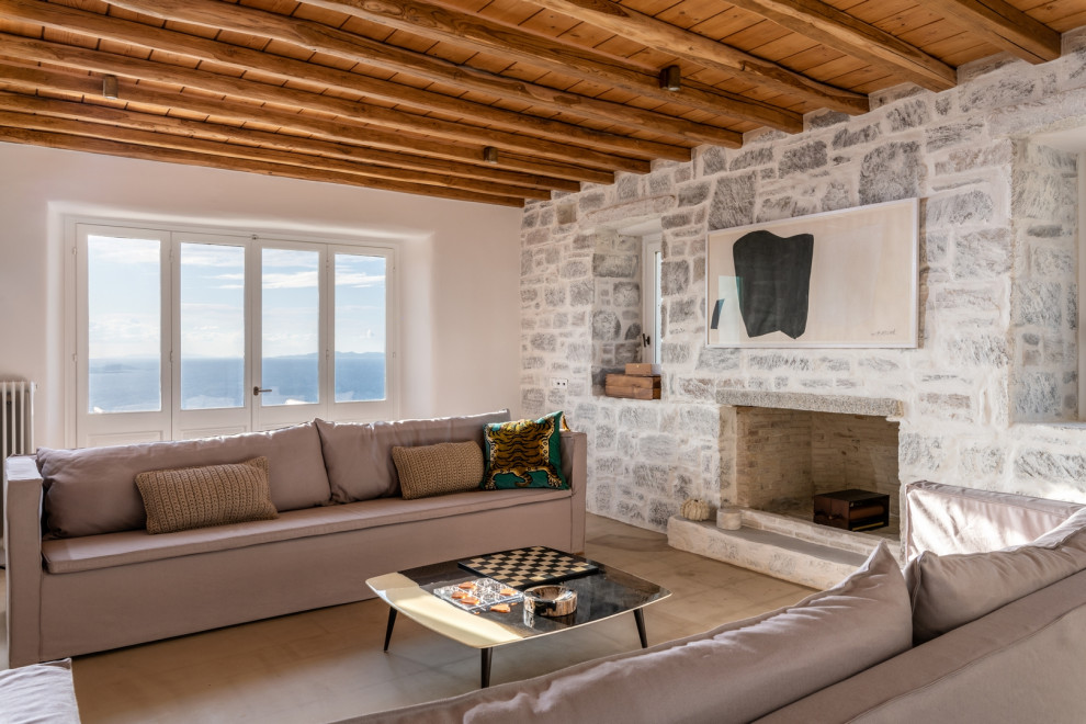 Exemple d'un salon méditerranéen avec une cheminée standard, un manteau de cheminée en pierre, un plafond en bois, poutres apparentes, un mur en parement de brique, un mur blanc et un sol gris.