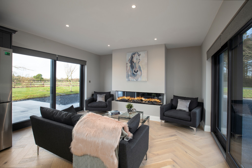 Esempio di un soggiorno design di medie dimensioni e aperto con pareti grigie, pavimento in legno massello medio, camino ad angolo e pavimento grigio