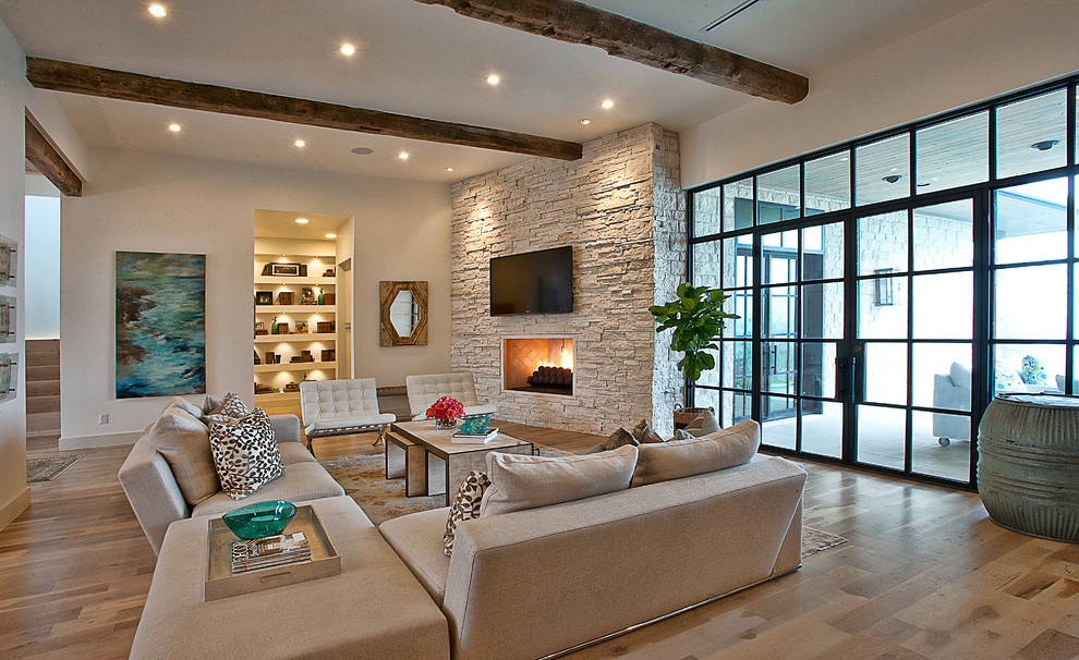 Cette photo montre un salon chic avec un mur blanc, un sol en bois brun, une cheminée d'angle, un téléviseur fixé au mur et un mur en pierre.