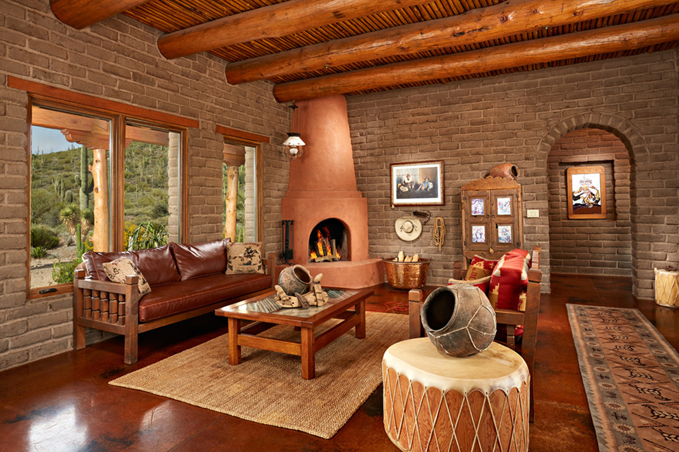 フェニックスにある広いサンタフェスタイルのおしゃれなリビング (コーナー設置型暖炉、漆喰の暖炉まわり、茶色い壁、コンクリートの床、テレビなし) の写真