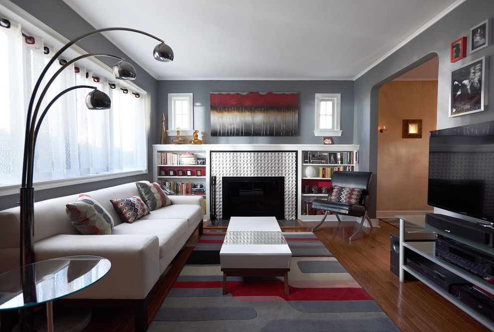 Immagine di un piccolo soggiorno moderno chiuso con pareti grigie, pavimento in legno massello medio, camino classico, cornice del camino piastrellata e TV autoportante