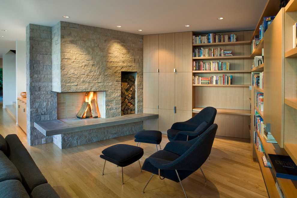 Cette image montre un salon design ouvert avec une bibliothèque ou un coin lecture, un sol en bois brun et un manteau de cheminée en pierre.