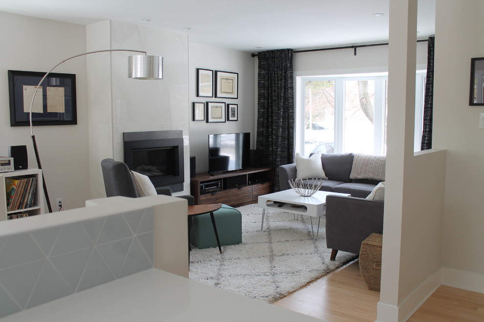 На фото: открытая гостиная комната среднего размера в стиле ретро с серыми стенами, светлым паркетным полом, стандартным камином, фасадом камина из плитки и отдельно стоящим телевизором