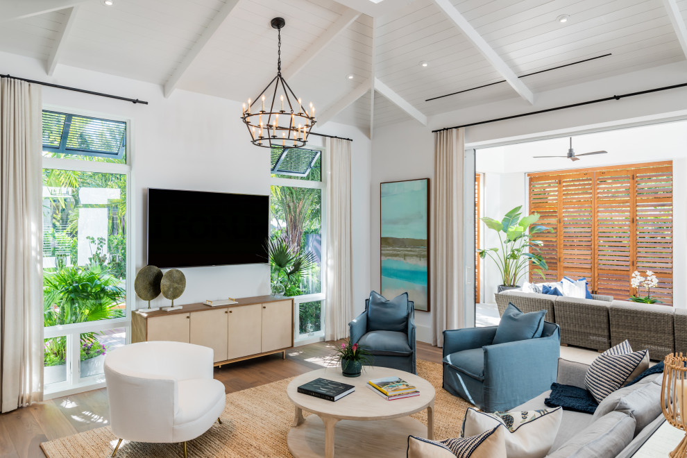 This is an example of a large beach style open plan living room in Miami with white walls, medium hardwood flooring, a wall mounted tv and brown floors.