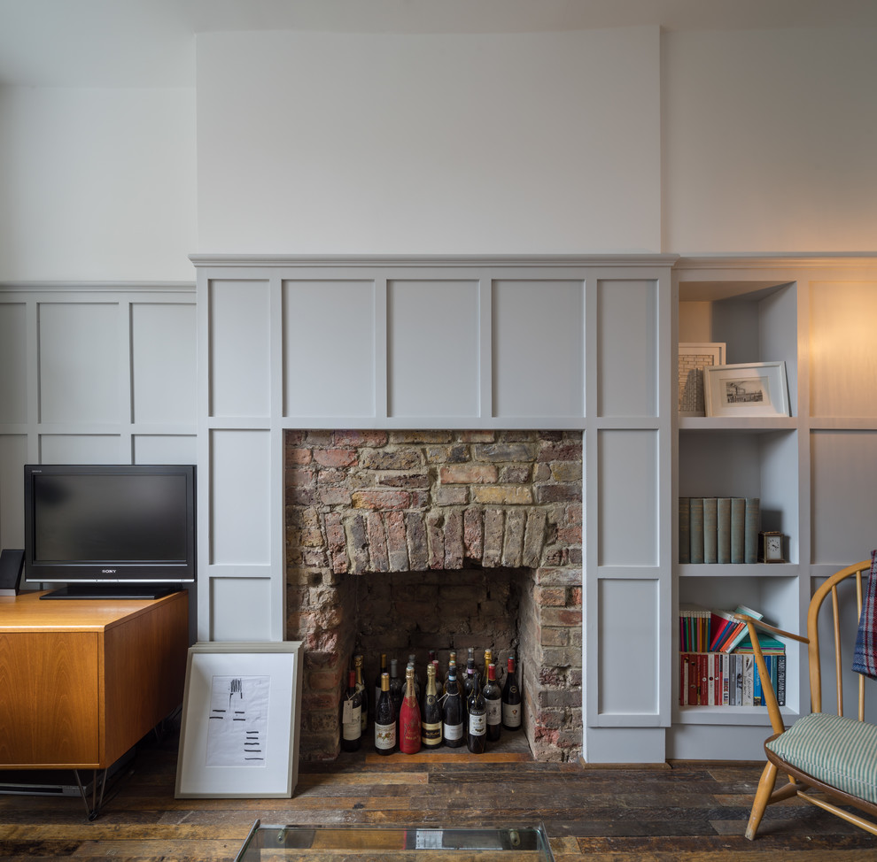 Mittelgroße Moderne Bibliothek mit grauer Wandfarbe, braunem Holzboden, Kamin, Kaminumrandung aus Backstein und freistehendem TV in London
