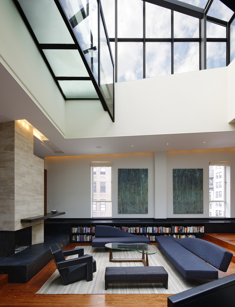 Geräumige, Fernseherlose Moderne Bibliothek im Loft-Stil mit weißer Wandfarbe, Tunnelkamin, braunem Holzboden und Kaminumrandung aus Stein in New York