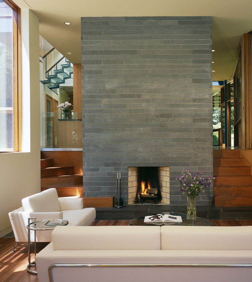 Diseño de salón abierto actual grande sin televisor con paredes blancas, suelo de madera en tonos medios y marco de chimenea de piedra